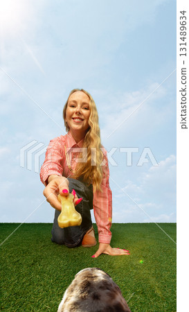 Cheerful woman reaching out with chew bone toy from dog playful eye level 131489634