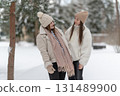 Two young women friends talking and laughing in a snowy park, dressed in warm winter clothing. Concept of friendship, happiness, and enjoying seasonal outdoor moments together. 131489900