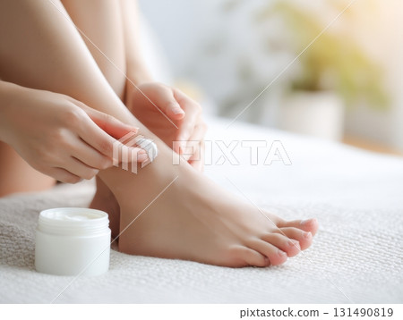 Young Asian woman focuses on smoothing cream onto her leg while sitting comfortably in a well-lit room 131490819