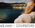 Over shoulder shot: blonde woman enjoying tranquil moment by quarry lake in Zakrzowek, Krakow, Poland, surrounded by stunning cliffs and lush greenery under beautiful sky. Woman relaxing near lake  131492540