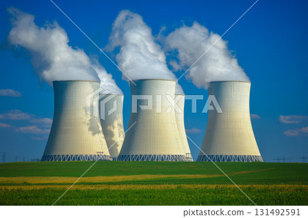 Cooling towers of a power plant emit steam against a bright blue sky, surrounded by green fields and distant power lines Cooling towers of a power plant emit steam against a bright blue sky, surrounded by green fields and distant power lines 131492591
