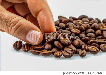A hand picks up freshly roasted coffee beans from a scattered pile, ready for brewing at home. The rich brown color shines 131492689