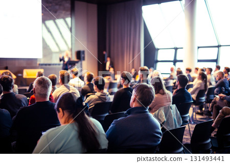 Speaker giving a talk in conference hall at business event. Rear view of unrecognizable people in audience at the conference hall. Business and entrepreneurship concept 131493441