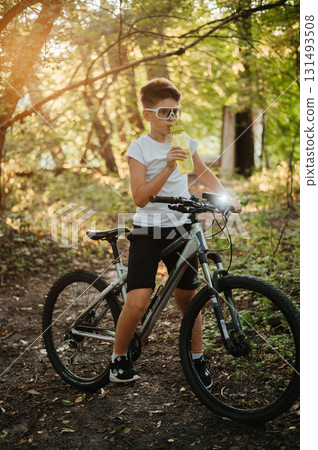 A Young Boy Joyfully Riding His Bicycle Through Beautiful Nature while Enjoying a Refreshing Drink 131493508