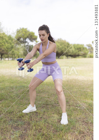 Woman exercising outdoors doing squats with dumbbells 131493881