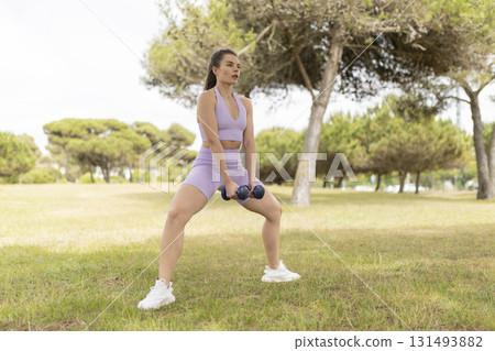 Woman exercising outdoors doing squats with dumbbells 131493882