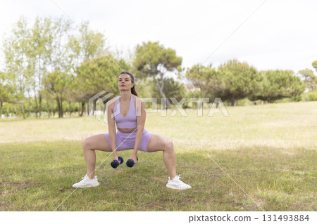 Woman exercising outdoors doing sumo squats dumbbells 131493884