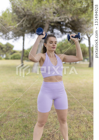 Young woman training with dumbbells in outdoor park Young woman training with dumbbells in outdoor park 131494028