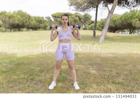 Woman exercising outdoors doing strength training with dumbbells Woman exercising outdoors doing strength training with dumbbells 131494031