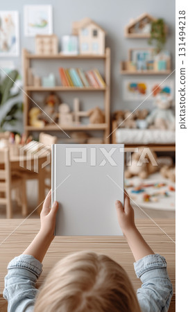 Child little blonde girl hold in hands closed kids book with a blank front cover in nursery room. childhood and reading concept mockup 131494218
