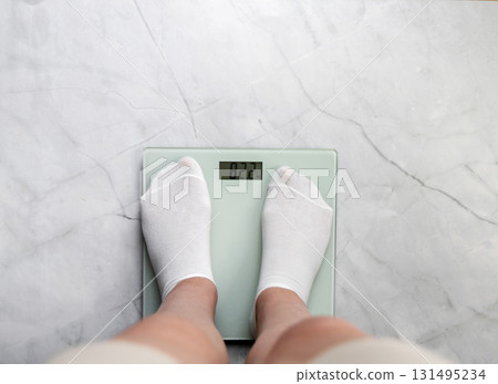 Feet in white socks stand on scales. Weight loss and diet concept. Feet in white socks stand on scales. Weight loss and diet concept. 131495234