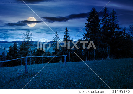 countryside scenery with meadow in mountains at night. wide rolling rural landscape with wooden fence on green field and forested hills in autumn in full moon light 131495370
