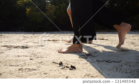 Male and female legs of pair walking on sandy beach. Bare feet of couple stepping along sand shore at sunny day. Lovers spending time together at resort. Concept of summer vacation or holiday Male and female legs of pair walking on sandy beach. Bare feet of couple stepping along sand shore at sunny day. Lovers spending time together at resort. Concept of summer vacation or holiday 131495548
