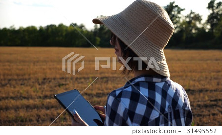 Adult farmer using digital tablet at wheat meadow on sunny day. Female agronomist monitoring harvest at barley field. Beautiful scenic landscape. Concept of agricultural business. Slow motion Adult farmer using digital tablet at wheat meadow on sunny day. Female agronomist monitoring harvest at barley field. Beautiful scenic landscape. Concept of agricultural business. Slow motion 131495552