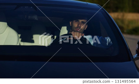 Handsome successful entrepreneur looking through windshield of modern electric car. Portrait of young smiling businessman in his innovative electrical vehicle. Slow motion Handsome successful entrepreneur looking through windshield of modern electric car. Portrait of young smiling businessman in his innovative electrical vehicle. Slow motion 131495564