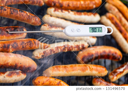 Raw sausages on barbecue with digital meat thermometer showing unsafe low temperature Raw sausages on barbecue with digital meat thermometer showing unsafe low temperature 131496570