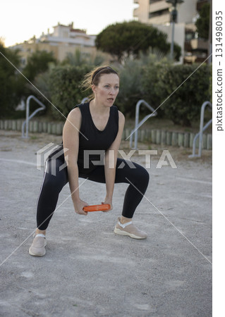 Woman exercising outdoors doing squats with weight 131498035