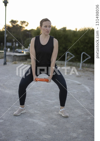 Woman exercising outdoors doing squats with fitness accessory 131498036