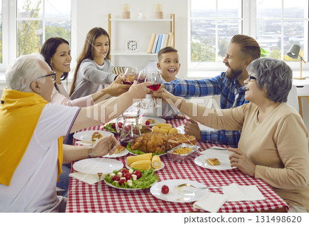 Joyful friendly multigenerational family clinking wine glasses during Thanksgiving celebration. 131498620