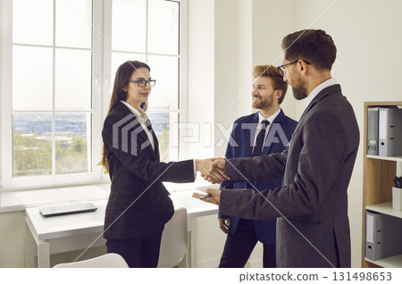 Business people standing in office making deal. Man shaking hands with woman finishing meeting. Business people standing in office making deal. Man shaking hands with woman finishing meeting. 131498653