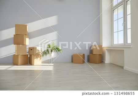 Unpacked cardboard boxes are stacked on the floor in the empty room in new apartment. 131498655
