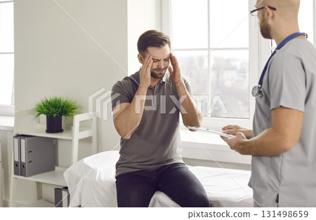 Young male patient is suffering from headache and asking doctor at clinic for help 131498659