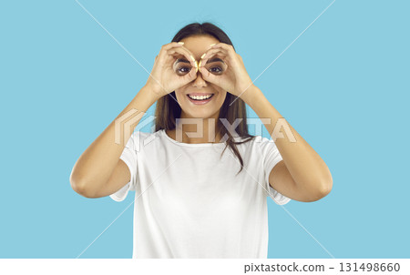 Happy beautiful young woman doing binoculars gesture, looking in distance and smiling 131498660