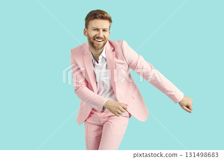 Young happy funny man in pink suit having fun isolated on studio blue background. 131498683