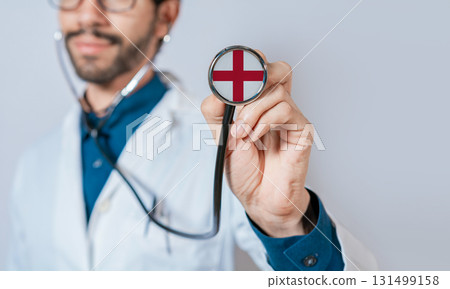 Doctor holding stethoscope with England flag. England health and care concept. England flag on stethoscope Doctor holding stethoscope with England flag. England health and care concept. England flag on stethoscope 131499158