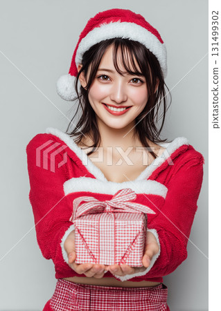 A woman in a Santa costume smiles and offers a present | Perfect for Christmas gift giving 131499302