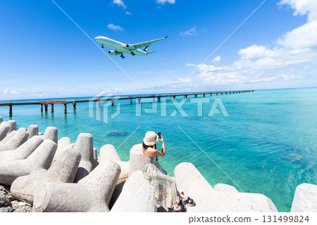 Miyako's spectacular view: A young woman and an airplane at 17 End Beach in front of Shimojishima Airport 131499824