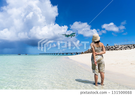 A young woman in a one-piece dress looking up at an airplane on an emerald beach 131500088