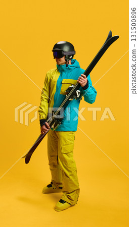 Skier posing with crossed skis in studio on yellow background 131500896