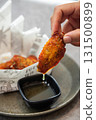 Pick up a herb roasted chicken wing snack with your hand and dip it into yuzu sauce 131500899