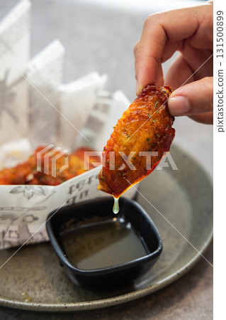 Pick up a herb roasted chicken wing snack with your hand and dip it into yuzu sauce Pick up a herb roasted chicken wing snack with your hand and dip it into yuzu sauce 131500899