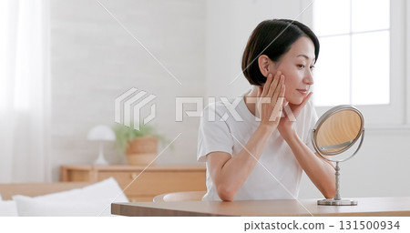 Middle-aged woman doing skin care while looking in the mirror 131500934