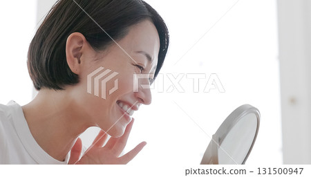 Middle-aged woman doing skin care while looking in the mirror Middle-aged woman doing skin care while looking in the mirror 131500947