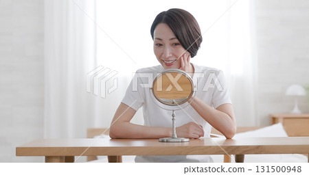 Middle-aged woman doing skin care while looking in the mirror Middle-aged woman doing skin care while looking in the mirror 131500948