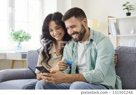 Smiling couple at home using smartphone and credit card for online shopping 131501248