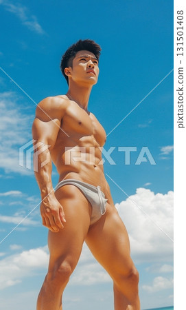 Fit Asian man in swim shorts standing on a tropical beach with a clear blue sky 131501408