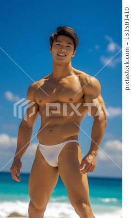 Fit Asian man in swim shorts standing on a tropical beach with a clear blue sky 131501410