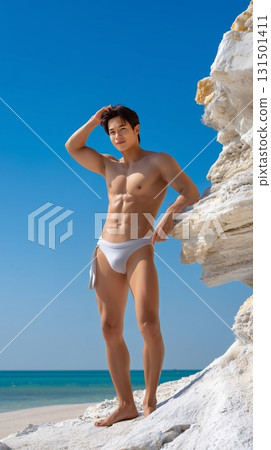 Fit Asian man in swim shorts standing on a tropical beach with a clear blue sky 131501411