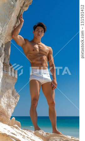 Fit Asian man in swim shorts standing on a tropical beach with a clear blue sky 131501412
