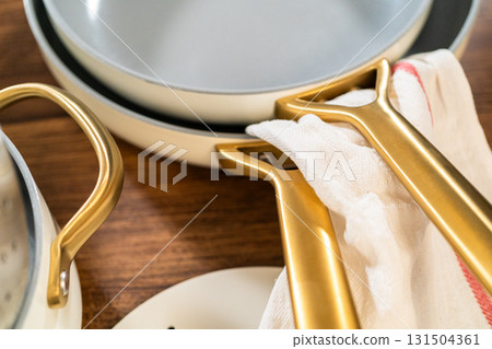 Overhead shot of two stacked gray ceramic pans with luxurious golden handles placed on kitchen towels. A soft lighting setup enhances the texture and tone of the cookware and fabrics. 131504361