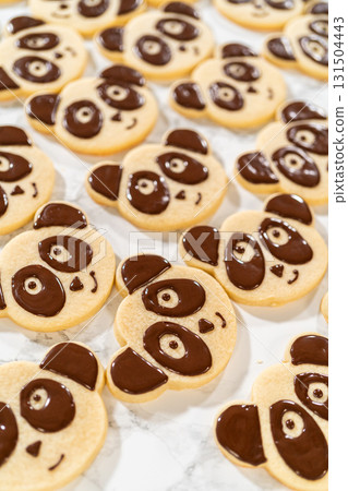 Overhead view of a batch of panda cookies with completed chocolate icing designs for the Chocolate Royal Icing Recipe. Each cookie features a cute panda face, giving a uniform and adorable look. 131504443