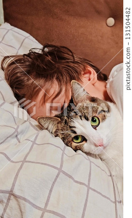 Teenage boy and a cat. Handsome guy hugs his cat while sitting on the couch. teenage boy on the couch is petting his cat. Vertical 131504482