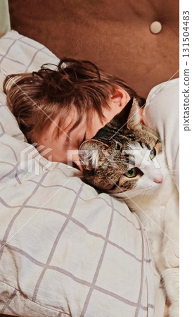 Teenage boy and a cat. Handsome guy hugs his cat while sitting on the couch. teenage boy on the couch is petting his cat. Vertical Teenage boy and a cat. Handsome guy hugs his cat while sitting on the couch. teenage boy on the couch is petting his cat. Vertical 131504483