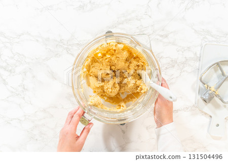 Top view of an electric mixer and bowls containing ingredients for Classic Sugar Cookie Dough. The mixer is placed over a bowl with partially mixed wet ingredients, while nearby bowls hold flour and a 131504496