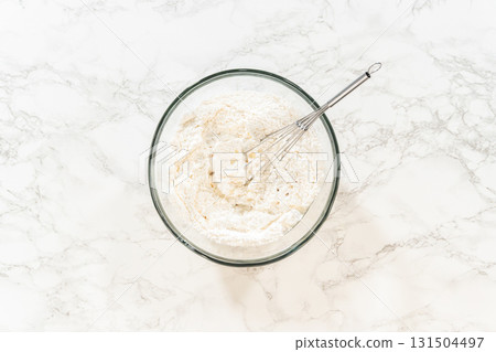 A bowl of partially mixed Simple White Royal Icing on a marble countertop, showing the whisking process to combine all ingredients. A bowl of partially mixed Simple White Royal Icing on a marble countertop, showing the whisking process to combine all ingredients. 131504497