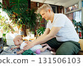 Young father supporting baby laying on the sofa teaching him to lay on tummy and hold his head up and roll over on tummy. Sensory tactile activities. Baby care. Parenthood and fatherhood. 131506103